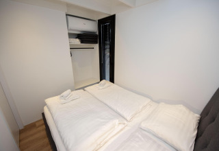 Dormitorio moderno en la casa flotante 'De Waterparel' en Welcome In - Friesland, Países Bajos, con cama y armario abierto.