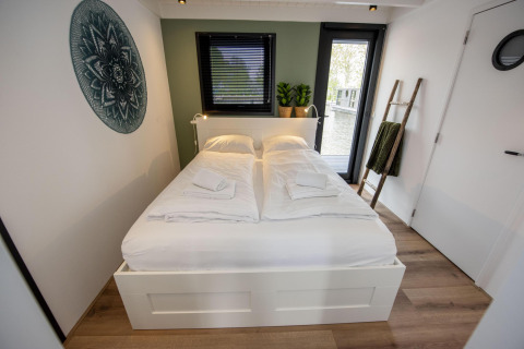 Dormitorio moderno en la casa flotante 'De Waterparel' con cama doble y vista al agua desde la ventana.
