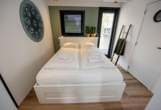 Moderne slaapkamer op woonboot 'De Waterparel' met dubbel bed, decoratieve ladder en waterzicht.