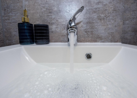 Grifo abierto llenando un lavabo en la casa flotante 'De Waterparel' en Welcome In - Friesland, Holanda.