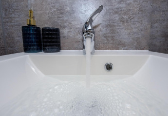 Grifo abierto llenando un lavabo en la casa flotante 'De Waterparel' en Welcome In - Friesland, Holanda.