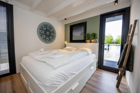 Dormitorio moderno en la casa flotante De Waterparel, con cama grande, decoración minimalista y vista al agua.