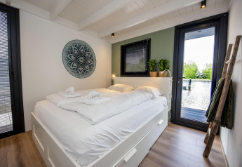 Dormitorio moderno en la casa flotante De Waterparel, con cama grande, decoración minimalista y vista al agua.