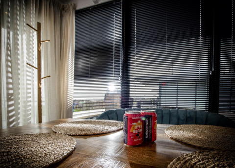 Área de estar en la casa flotante De Waterparel en Friesland con mesa, latas y persianas en las ventanas.