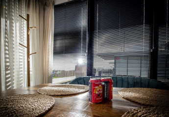 Área de estar en la casa flotante De Waterparel en Friesland con mesa, latas y persianas en las ventanas.