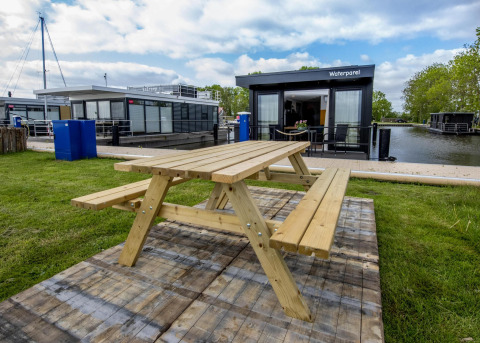 Mesa de picnic de madera sobre césped junto a casas flotantes, incluida 'De Waterparel', en Friesland, Países Bajos.