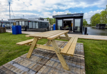 Mesa de picnic de madera sobre césped junto a casas flotantes, incluida 'De Waterparel', en Friesland, Países Bajos.