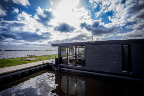 Casa flotante moderna 'De Waterparel' en Welcome In - Friesland, Países Bajos, junto a un lago y mesa picnic.