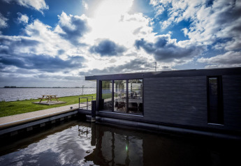 Casa flotante moderna 'De Waterparel' en Welcome In - Friesland, Países Bajos, junto a un lago y mesa picnic.