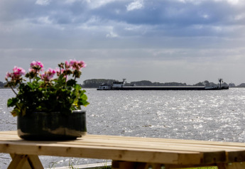 Vista desde la casa flotante 'De Waterparel' con flores en primer plano y una barcaza en el agua en Frisia.