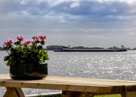 Vista desde la casa flotante 'De Waterparel' con flores en primer plano y una barcaza en el agua en Frisia.