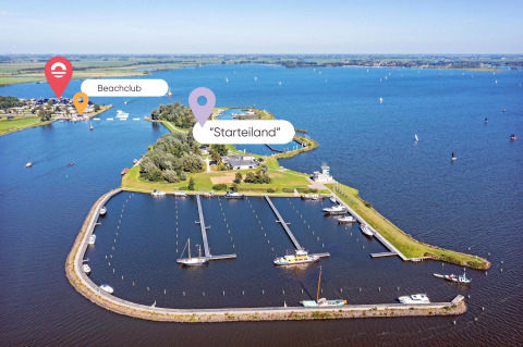 Vista aerea di un glamping sull’acqua con porto turistico, zone verdi e beach club in lontananza.