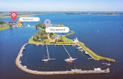 Luchtfoto van glamping bij het water met jachthaven, groen eiland en beachclub op de achtergrond.