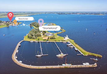 Vista aerea di un glamping sull’acqua con porto turistico, zone verdi e beach club in lontananza.
