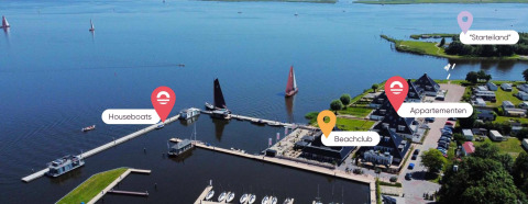 Luftaufnahme einer Glamping-Unterkunft mit Hausbooten, Apartments, Beachclub und Startinsel am Wasser.