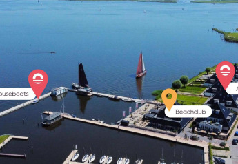 Vue aérienne d’un hébergement glamping avec péniches, appartements, beach club et île de départ près d’un lac.