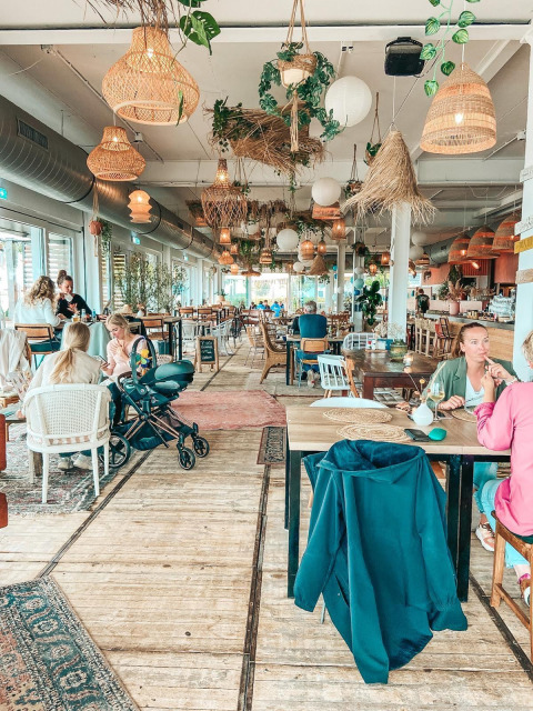 Ristorante glamping luminoso e accogliente con lampade sospese, piante e ospiti rilassati ai tavoli.