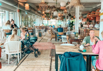 Restaurant de glamping lumineux et accueillant, décoré de plantes, lampes suspendues et clients détendus.