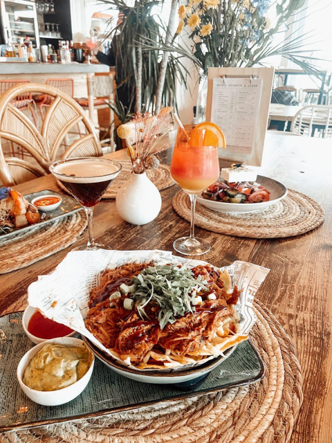 Leckeres Essen mit Cocktails, Nachos und Dips auf einem Holztisch in einer stilvollen Glamping-Unterkunft.