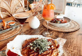 Leckeres Essen mit Cocktails, Nachos und Dips auf einem Holztisch in einer stilvollen Glamping-Unterkunft.