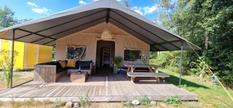 Hyggeligt safari-telt ved Zomerlicht i Holland med sofa, bord og terrasse omgivet af natur.