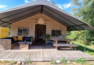 Hyggeligt safari-telt ved Zomerlicht i Holland med sofa, bord og terrasse omgivet af natur.