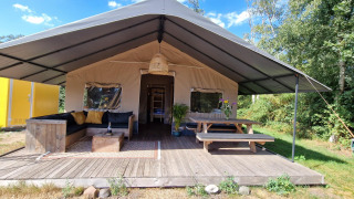 Safari-Zelt bei Zomerlicht in den Niederlanden mit Sofa, Picknicktisch und Terrasse im Grünen.