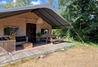 Safaritent bij Zomerlicht in Nederland met houten terras, picknicktafel, loungehoek en natuur.