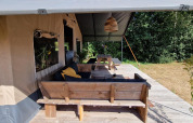 Cozy wooden terrace seating in front of a safari tent at Zomerlicht, Netherlands, surrounded by nature.