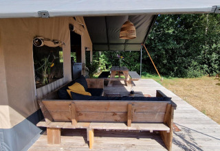 Area relax in legno davanti a una tenda safari a Zomerlicht, Paesi Bassi, immersa nella natura.