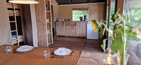 Spisebord med solskinsblomster og campingkøkken i en safaritelts hytte i Zomerlicht, Holland.