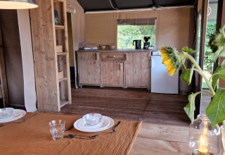 Spisebord med solskinsblomster og campingkøkken i en safaritelts hytte i Zomerlicht, Holland.