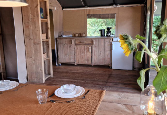 Essbereich mit Sonnenblumen und Holzküche in einem Safarizelt bei Zomerlicht in den Niederlanden.