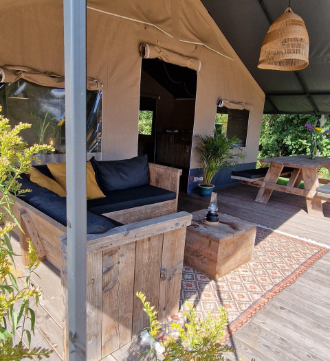 Zona lounge all’aperto nella tenda safari di Zomerlicht, Paesi Bassi, con arredi rustici in legno e tappeto.