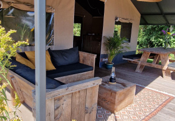 Espace salon extérieur sous tente safari à Zomerlicht, Pays-Bas avec meubles en bois rustiques et tapis.