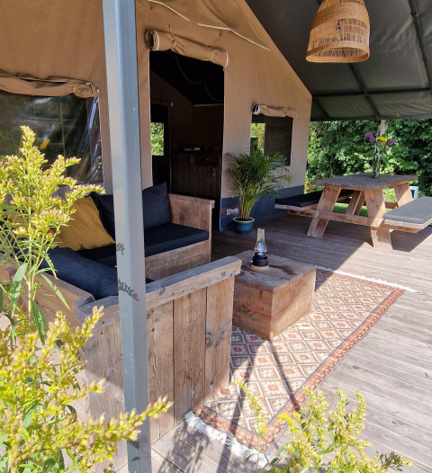 Tienda safari en Zomerlicht, Países Bajos, con muebles de madera, alfombra, lámpara y mesa de picnic.