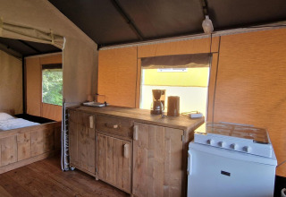 Interno di tenda safari presso Zomerlicht, Paesi Bassi, con angolo cottura, fornello, macchina da caffè e letto.