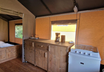 Intérieur d'une tente safari à Zomerlicht, Pays-Bas, avec kitchenette, cuisinière, cafetière et lit.