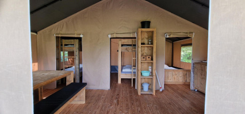 Vista interior de una tienda safari en Zomerlicht, Países Bajos, con muebles de madera y camas acogedoras.