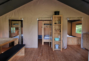 Vista interior de una tienda safari en Zomerlicht, Países Bajos, con muebles de madera y camas acogedoras.
