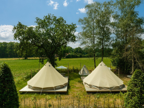 To tipi-telte på trædæk på en grøn eng ved Holiday Park Mölke i Holland under blå himmel.