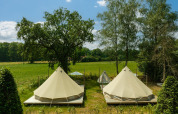 Two teepee tents on wooden decks in a sunny meadow at Holiday Park Mölke, Netherlands, with trees.