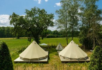 To tipi-telte på trædæk på en grøn eng ved Holiday Park Mölke i Holland under blå himmel.