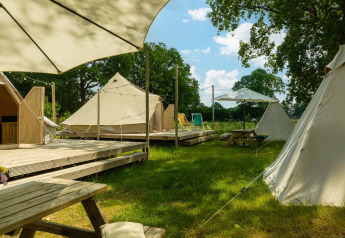 Area glamping con tende tipi, piattaforme in legno, tavoli da picnic e ombrelloni all'Holiday Park Mölke, Paesi Bassi.