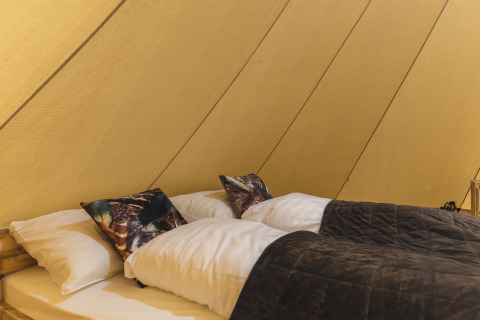 Interior de la tienda tipi Happy in the meadow con cama doble y cojines en Holiday Park Mölke.