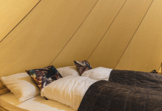 Interieur van de Happy in the meadow tipi tent met tweepersoonsbed en kussens bij Holiday Park Mölke.