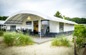 Safari Tent Villa en Holiday Park Duinhoeve, Países Bajos, rodeada de arena y vegetación bajo cielo nublado.
