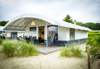 Safari Tent Villa bij Holiday Park Duinhoeve in Nederland, omringd door zand, gras en een bewolkte hemel.
