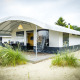 Safari Tent Villa au Holiday Park Duinhoeve, aux Pays-Bas, entourée de sable et de verdure sous un ciel nuageux.