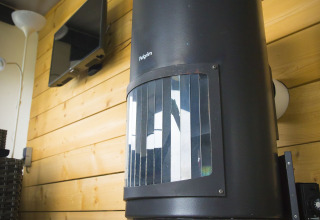 Zwarte houtkachel in Tent Villa, Holiday Park Duinhoeve, Nederland, met houten wand en tv.